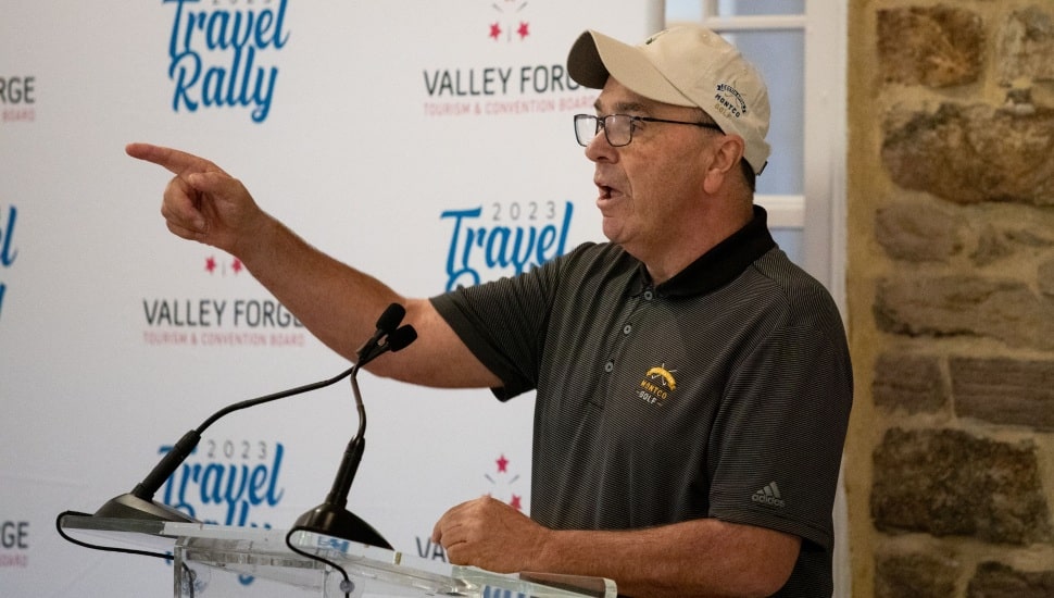 Mike Bowman, wearing a Montco Golf polo and cap, speaks passionately at a podium during the 2023 Travel Rally hosted by the Valley Forge Tourism & Convention Board.