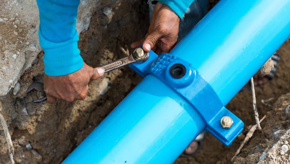 Man using a large wrench on water pipes. Construction site with new Water Pipes in the ground. Sewer pipes to repair or restore in street city.