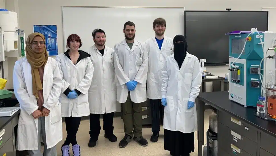 Group photo of six Montgomery County Community College Biotechnology students wearing white lab coats, standing together in a classroom setting.