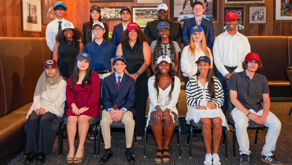 Group of high school seniors wearing hats of their colleges receive scholarships.