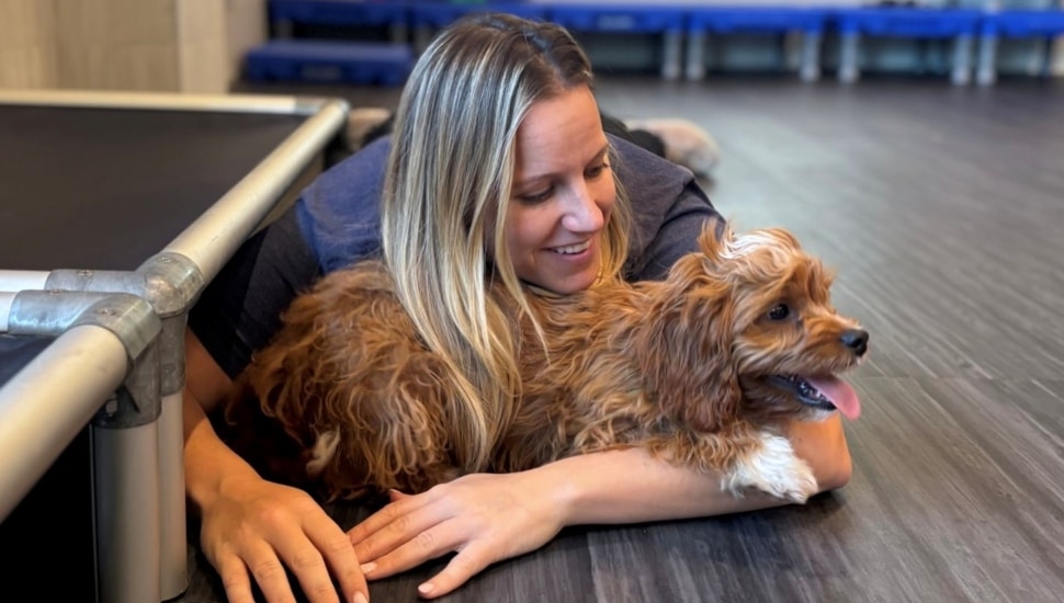Blond woman hugs her dog while lying in the floor.