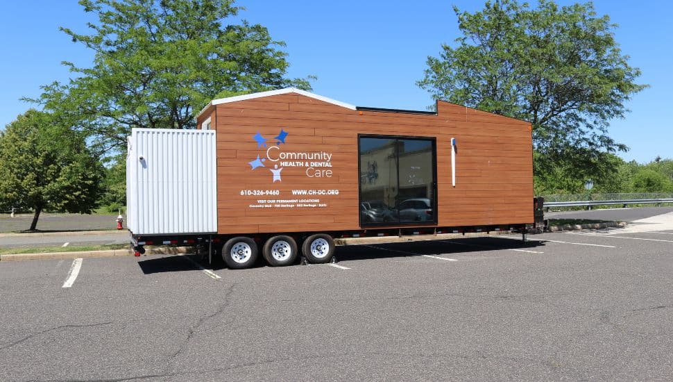 Community Health & Dental Care’s mobile dental unit parked in a lot, featuring wood paneling and the CHDC logo with contact information on the side.