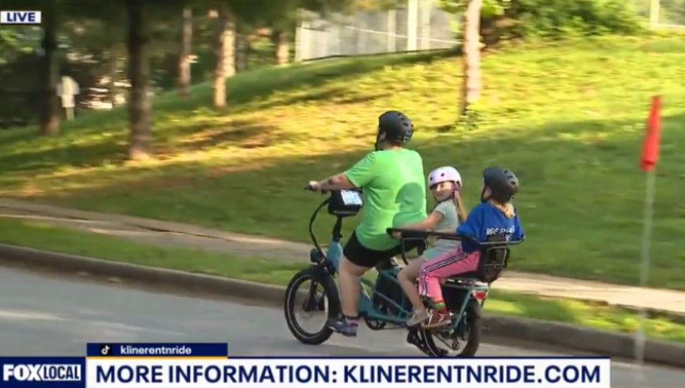 A mom rides an E-bike down the street with her two children.