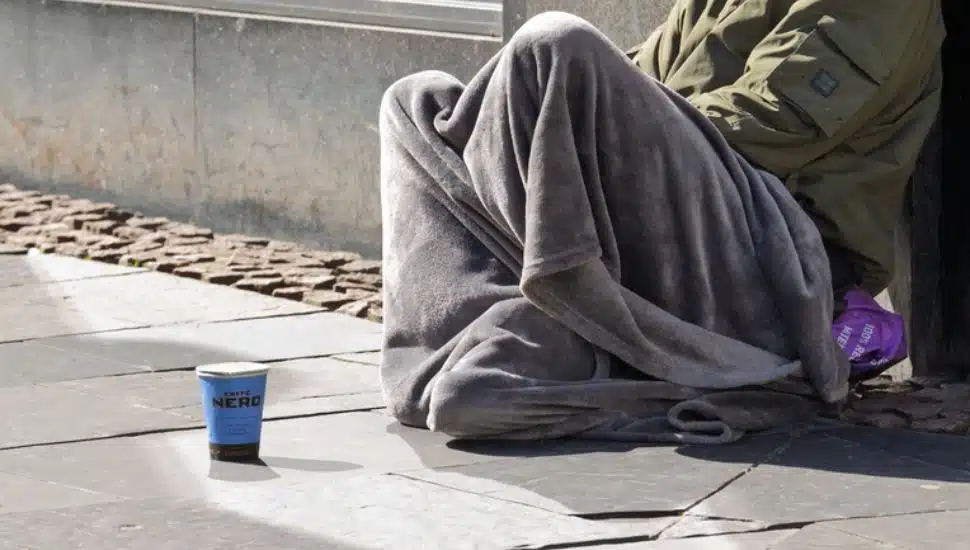 A homeless man sits on a street corner.