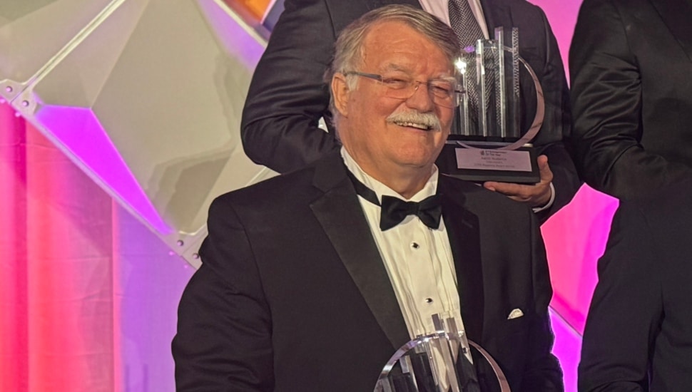 Older white male with gray hair and mustache in tuxedo receives award.