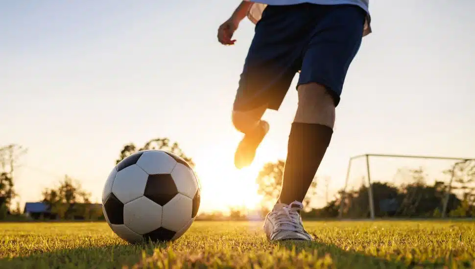 Close up shot of soccer player kicking ball. Action sport outdoors playing football for exercise at green grass field under the twilight sunset.