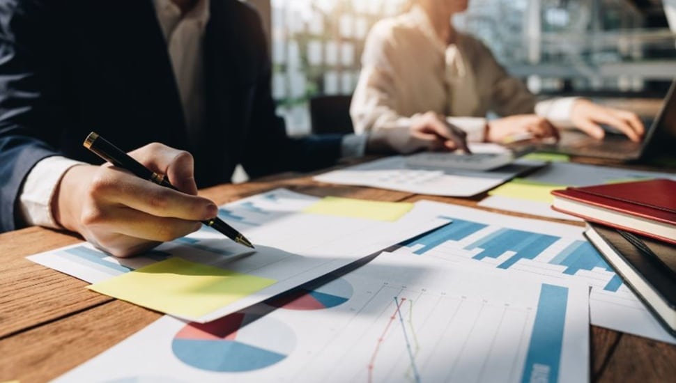 Business man and woman work with charts and other documents at a desk.