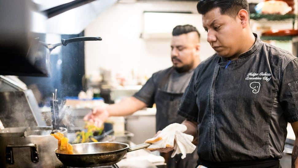 Executive Chef at The Blue Elephant cooking in a professional kitchen with another chef in the background, representing The Blue Elephant restaurant in Montgomery County.