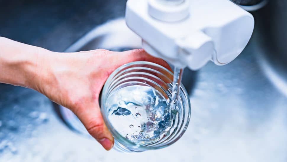 Close-up of a hand holding a glass under a faucet as clean water pours in, representing safe and sustainable water treatment.