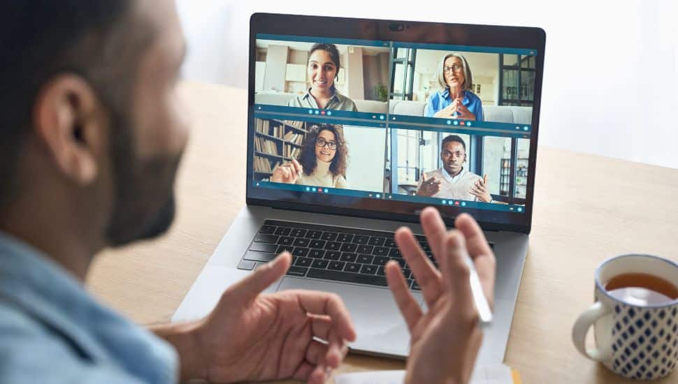 Indian businessman having virtual team meeting group call chatting with diverse people in a video conference call on computer.