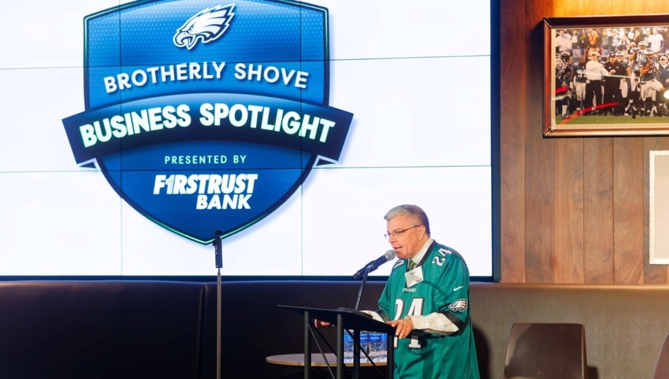 Older man in football jersey speaks at a podium.