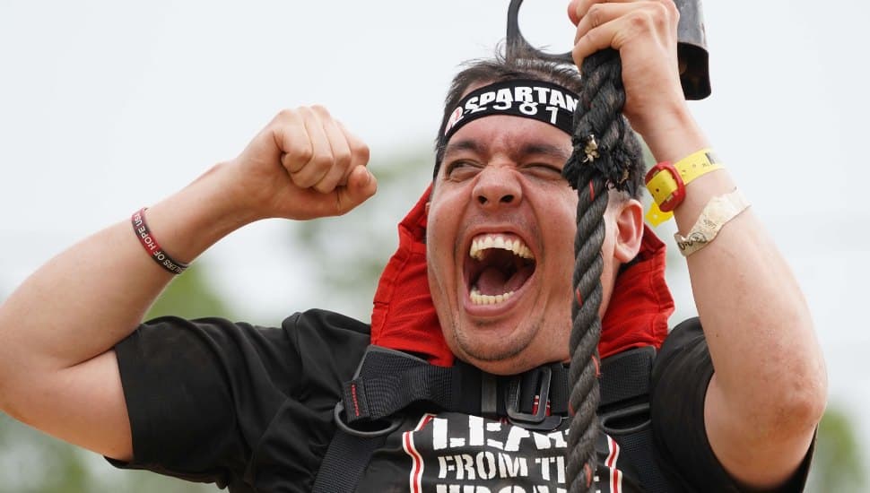 Kyle Keech, an adaptive athlete, raises his arms in celebration after completing the Spartan Race, supported by volunteers and the IM ABLE Foundation.