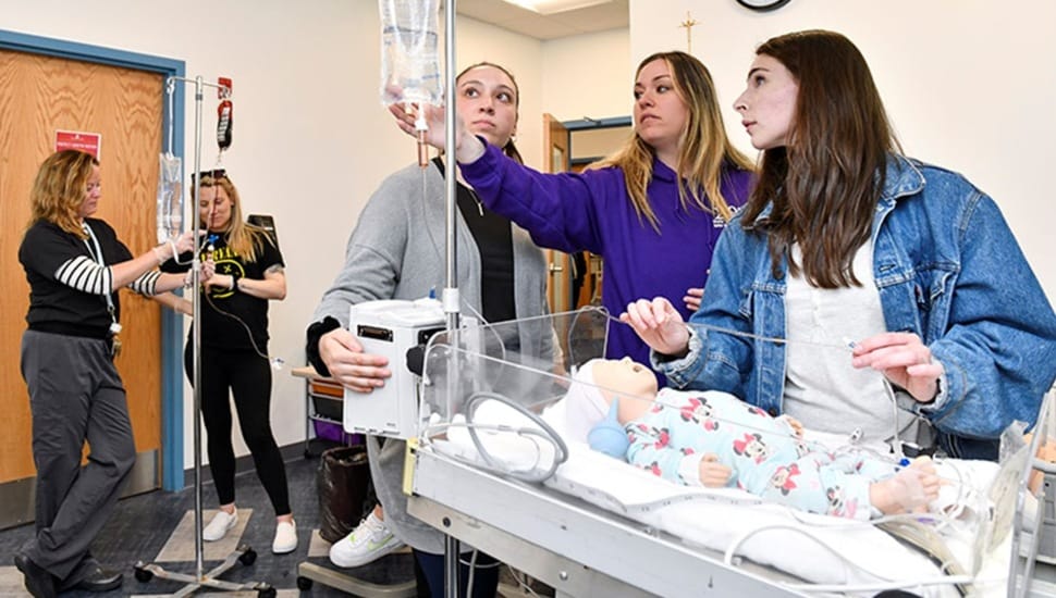 Female nursing students tend to baby doll patient.