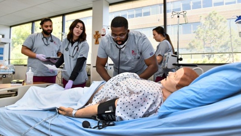 Four nursing students tend to doll patient.