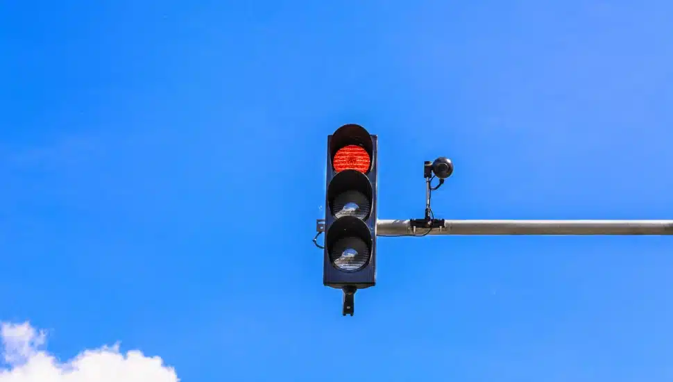 A traffic light and a surveillance camera on a pole mounted on the street.