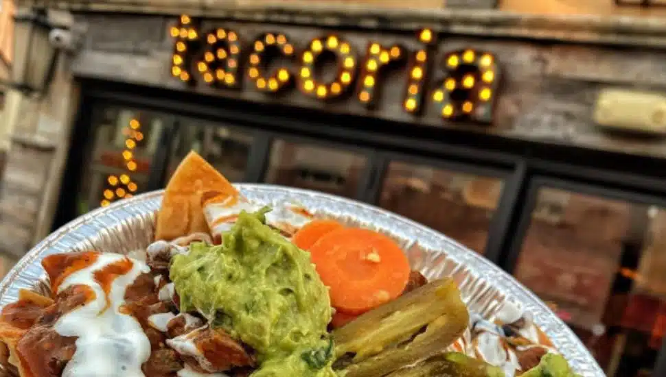 A closeup of a Mexican burrito bowl held up in front of a Tacoria location