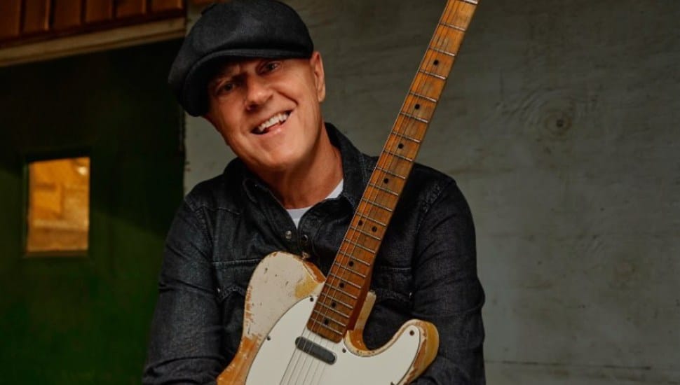 Tommy Conwell smiles with a guitar in his lap.