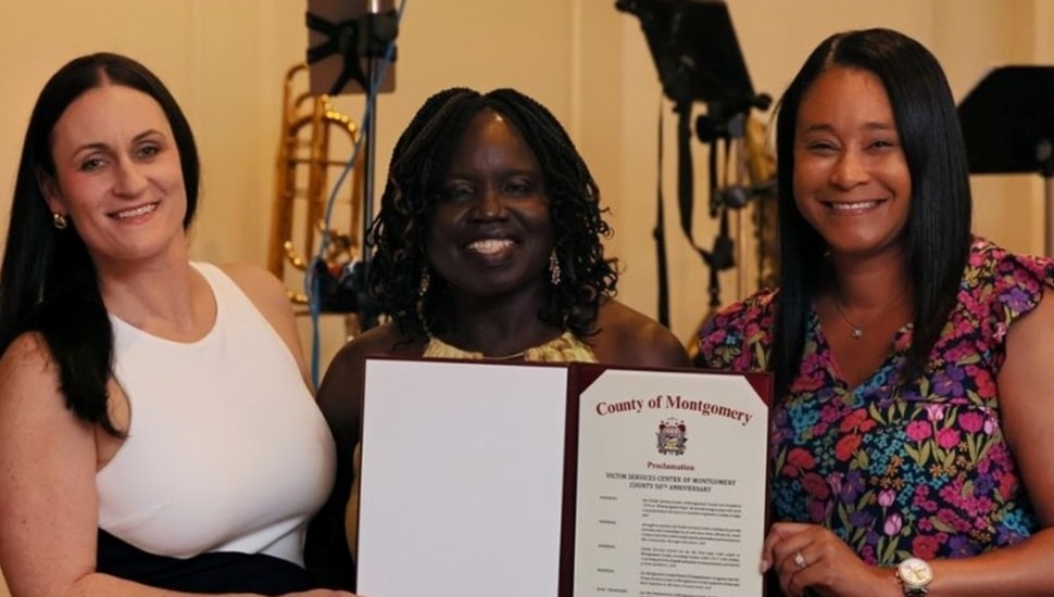 Three women pose for a group photo with a letter of recognition.