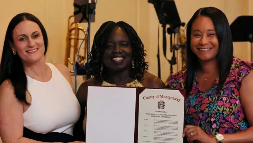 Three women pose for a group photo with a letter of recognition.