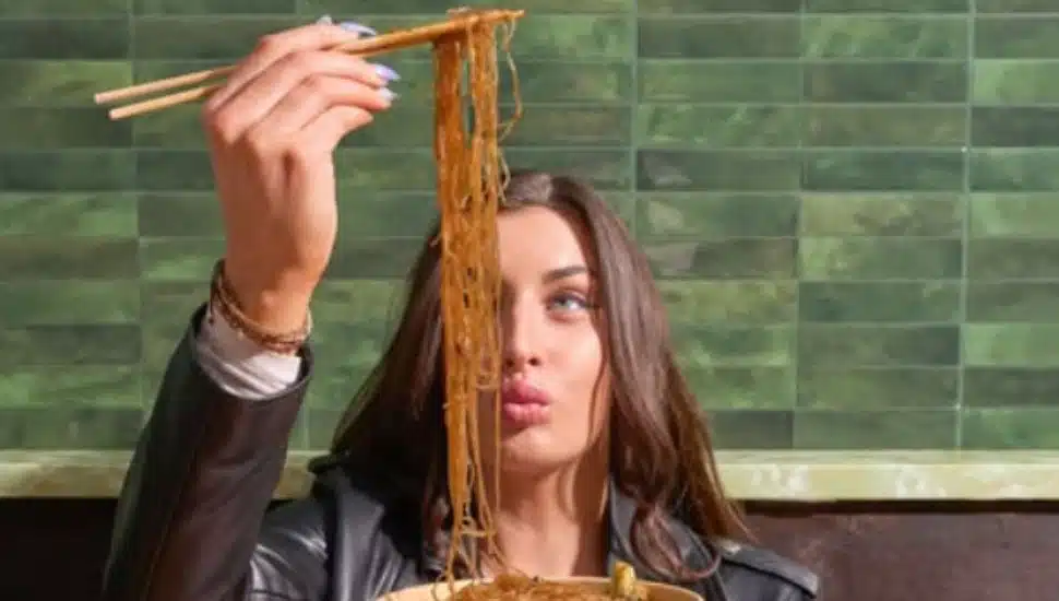 A woman holds up stir fry in front of her face with chopsticks.