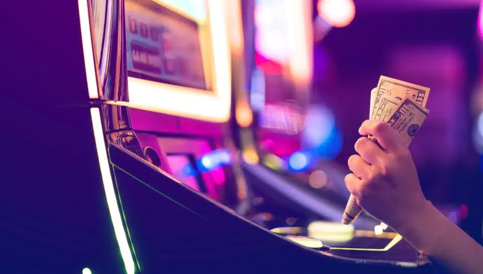 A female gambler holds money and is ready to win at slot machine.