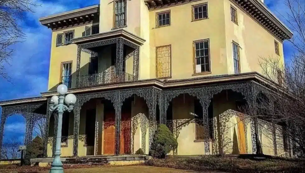 Front view of the historic Kennedy Supplee Mansion in Valley Forge, Pennsylvania, featuring ornate ironwork, boarded-up windows, and a weathered exterior—set against a vivid blue sky, highlighting the building’s Victorian architecture and current state before planned restoration.