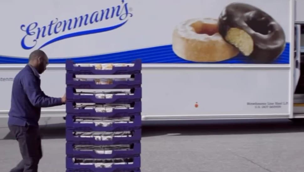 A Bimbos Bakeries employee pushes a cart filled with baked goods in front of a truck with the 'Entenmann's' logo brandished on the side.