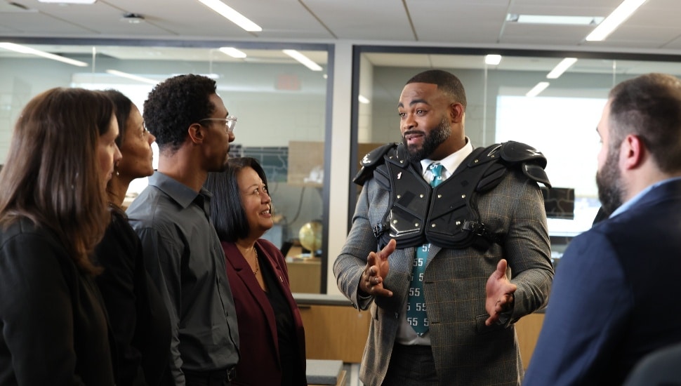 Football player in suit and should pads talks with bank employees.