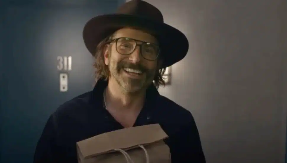 Bradley Cooper comes to the front door in glasses and a hat in the film, Is This Thing On?