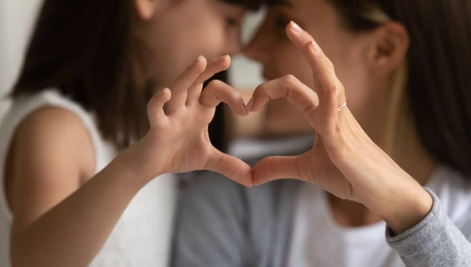 Mother and daughter make heart shape with hands.