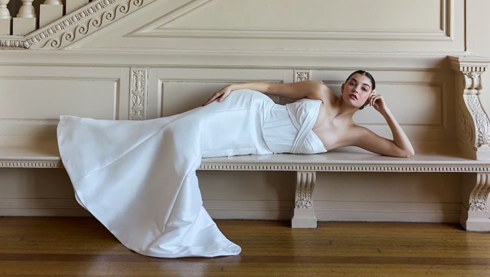 A bride lays across a bench in a wedding dress.