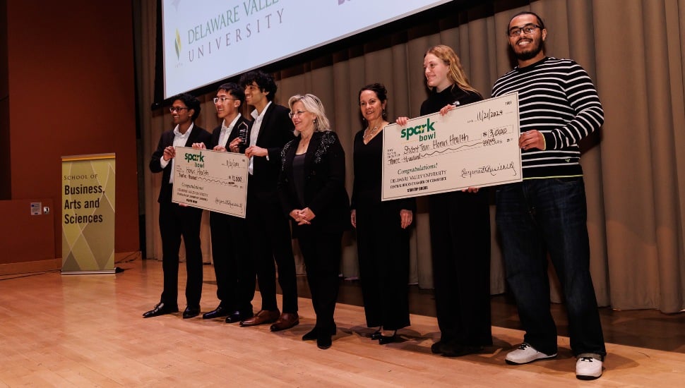 Student entrepreneurs hold giant check on stage.