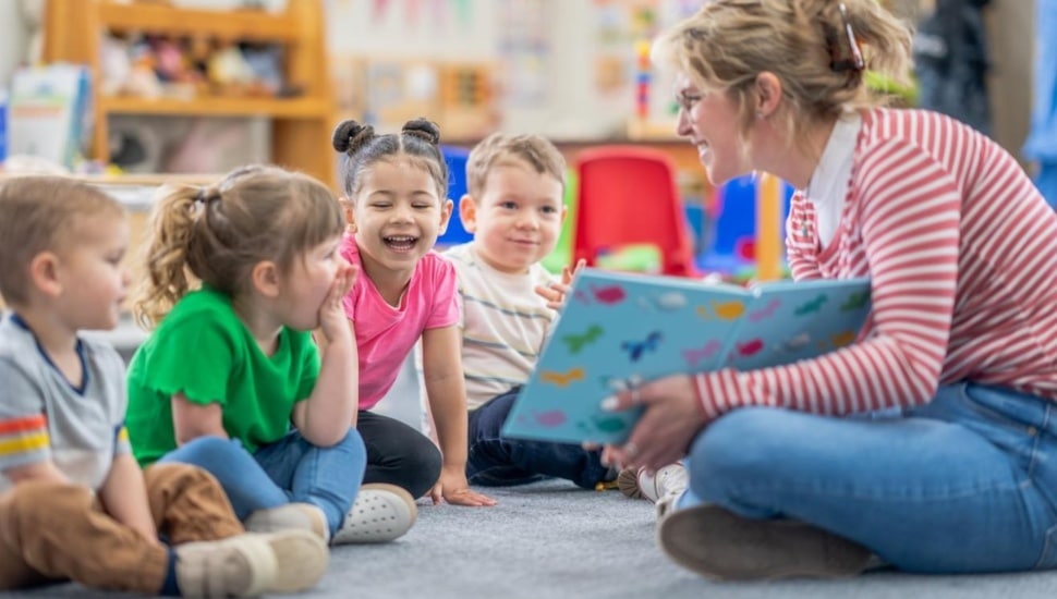 Young female kindergarten teacher reads to students at circle time.