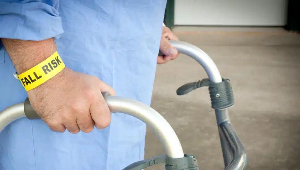 A patient walking with a walker wearing a fall risk bracelet and blue gown