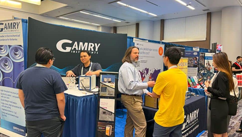 Men representing Gamry Instrument speaking with visitors at event.