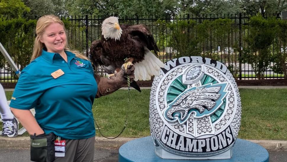 Elmwood Park Zoo's Laura Soder with Eagles mascot, Reggie, standing in front of a giant Super Bowl ring.