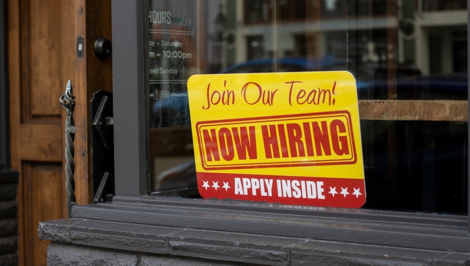 Now Hiring sign is seen at the storefront of a business.