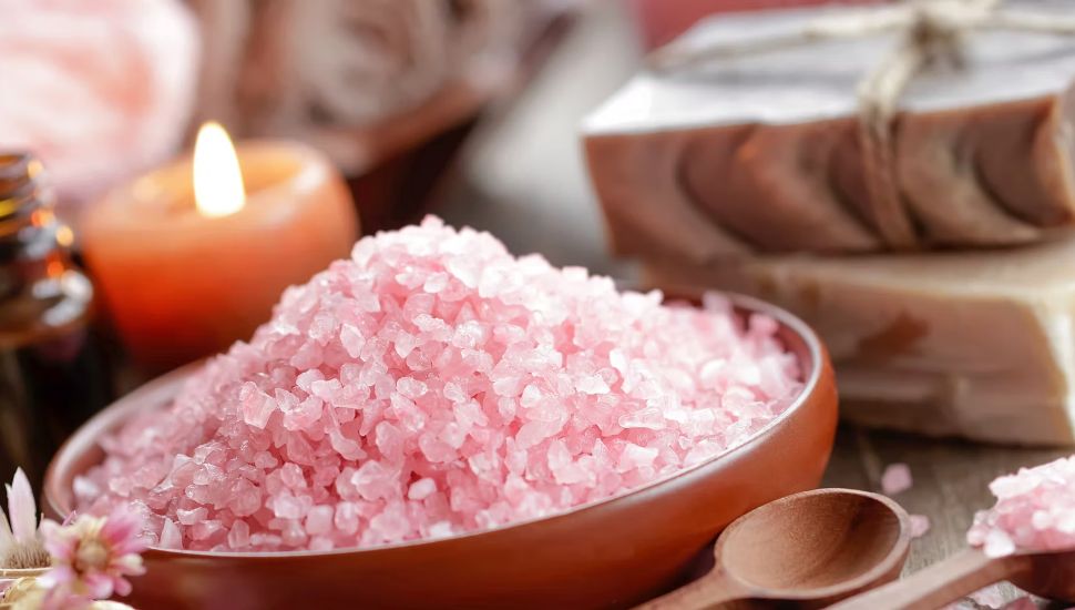 Pink Himalayan salt in a wooden bowl with a candle in the background.