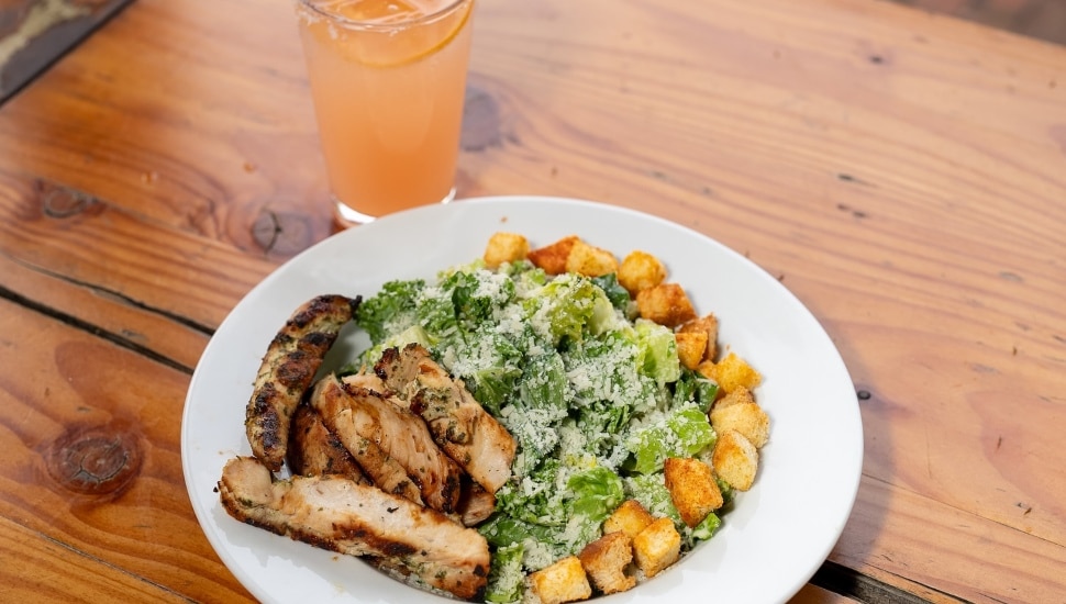 A caesar salad with grilled chicken and croutons, and a drink.