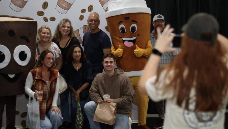 Group of festival attendees smiling for a photo with two costumed mascots — a chocolate bar and a coffee cup — at the Pennsylvania Chocolate & Coffee Festival in Oaks, Pennsylvania.