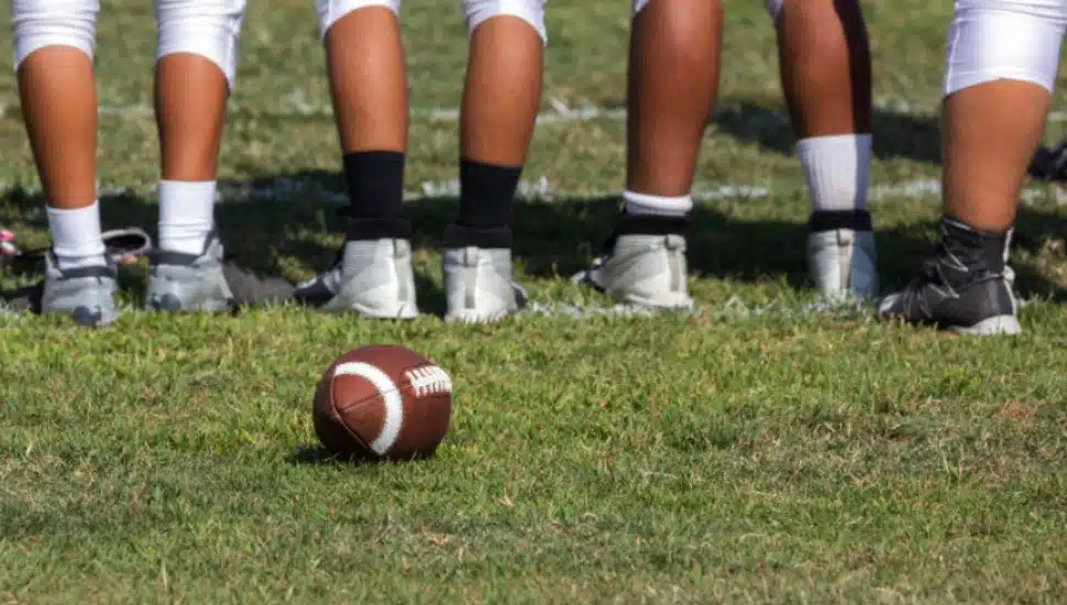 High school athletes stand on a field in front of a football.