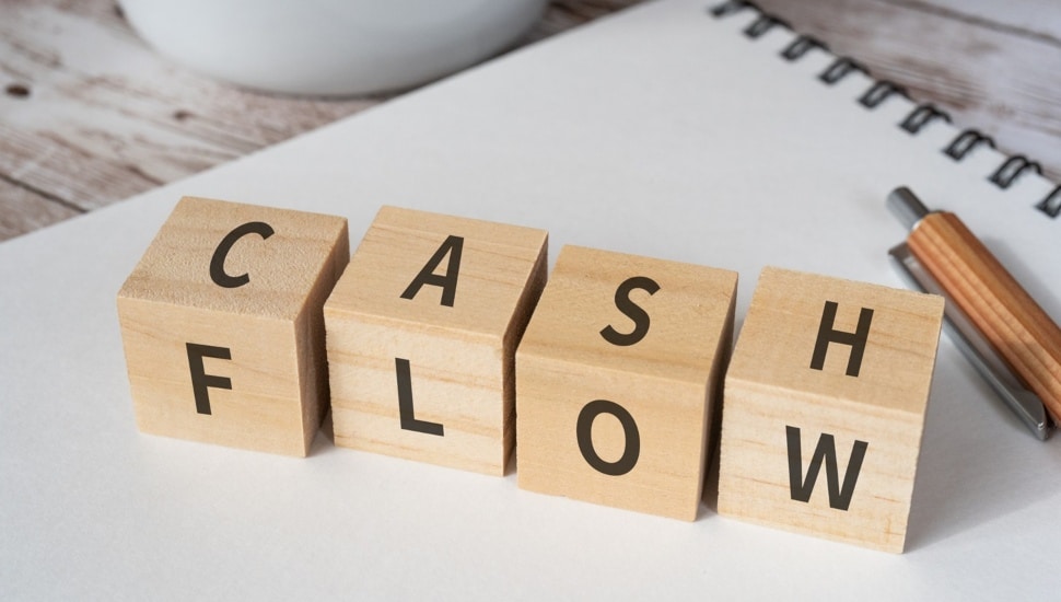 Wooden blocks with "CASH FLOW" text of concept, a pen, a notebook, and a cup.