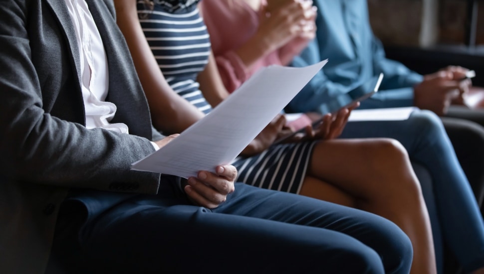Close up unrecognizable young multiracial people sitting in line on sofa with paper documents or modern technology gadgets, waiting for job interview or examination, human resources recruit concept.