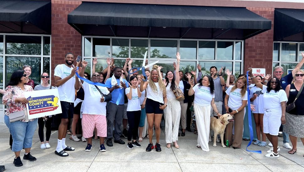 Tyneeha Rivers, founder of Nova Dawn Yoga & Pilates, smiles while standing in front of the studio’s entrance during the grand opening event in King of Prussia. She holds large ceremonial scissors after cutting the ribbon, surrounded by balloons and welcoming signage.