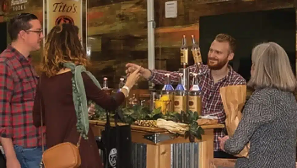 Festival attendees at TASTE! Philadelphia sampling craft spirits from a vendor booth, with bottles on display and a bartender serving drinks.