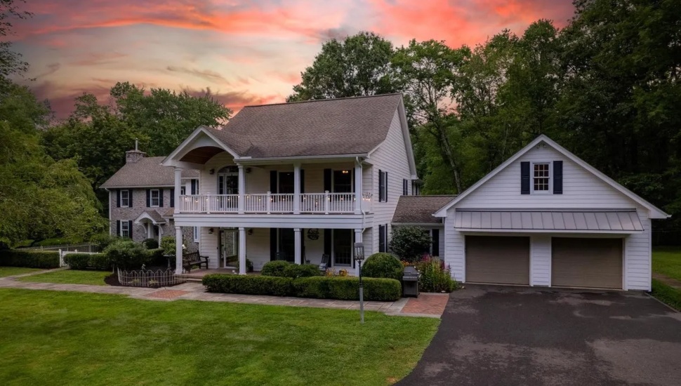 Estate with white siding and stone exterior on a manicured lawn at sunset.