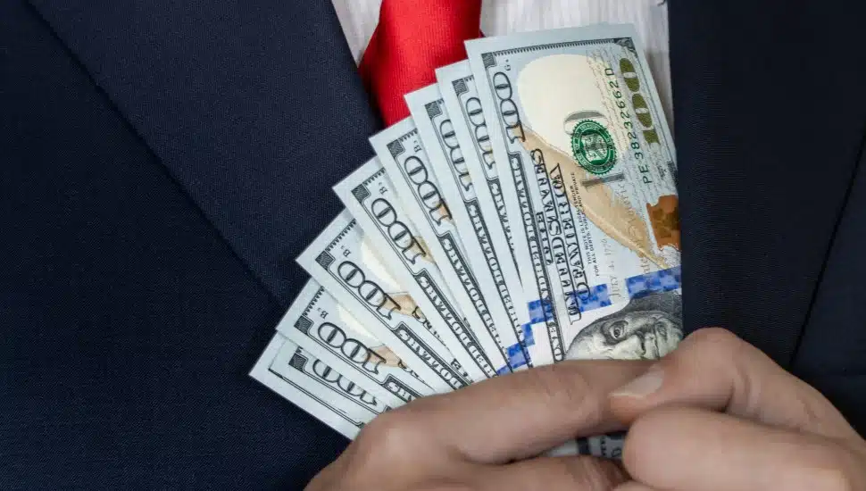 A wealthy man tucks hundred-dollar bills into his jacket pocket.