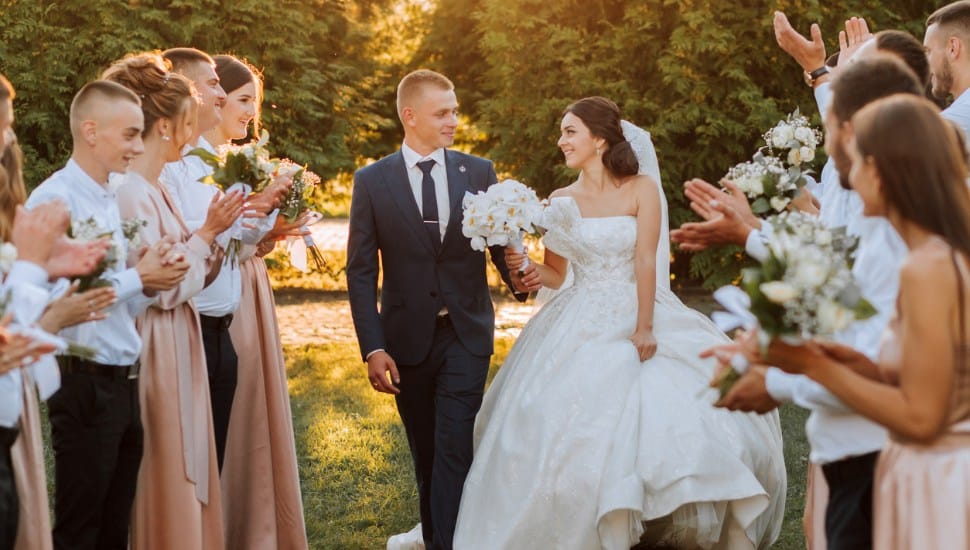 A bride and groom walk down the aisle after their wedding ceremony at sunset as friends and family celebrate.