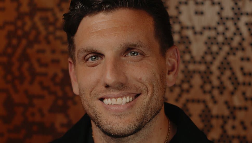 Comedian Chris Distefano smiling in a close-up portrait with a patterned background.