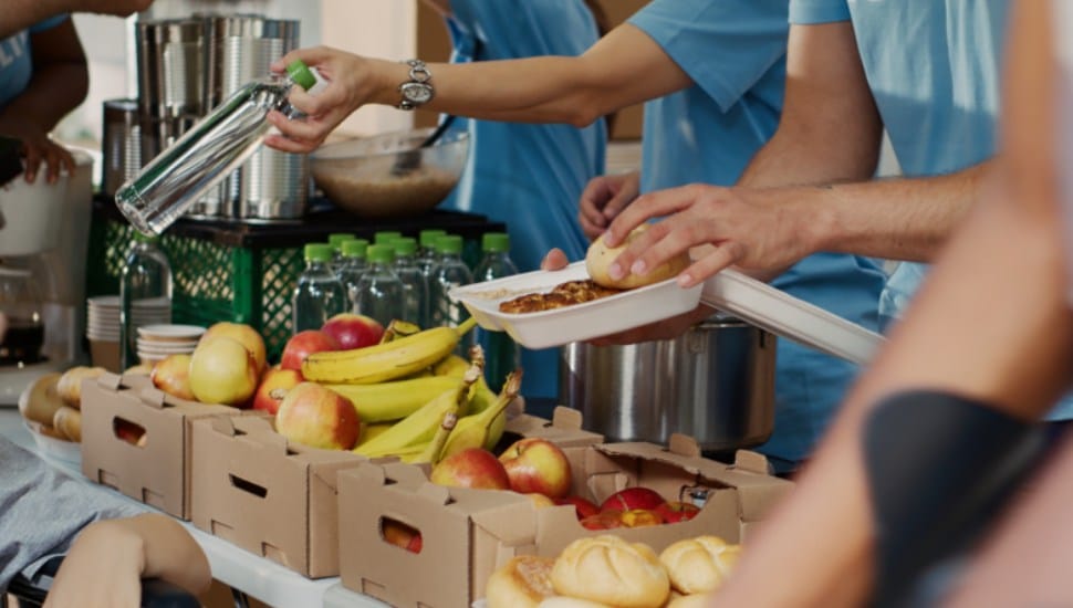 Multiethnic volunteers in blue t-shirt distributing fresh fruits and hot meals to less privileged.
